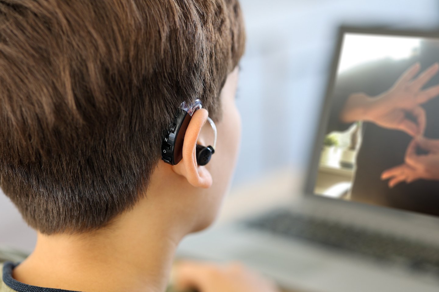 Deaf teenager boy Wearing Hearing Aid using Laptop. Disable student with disabilities deafness distancing learning online from home making communication hands language with teacher via Video call.